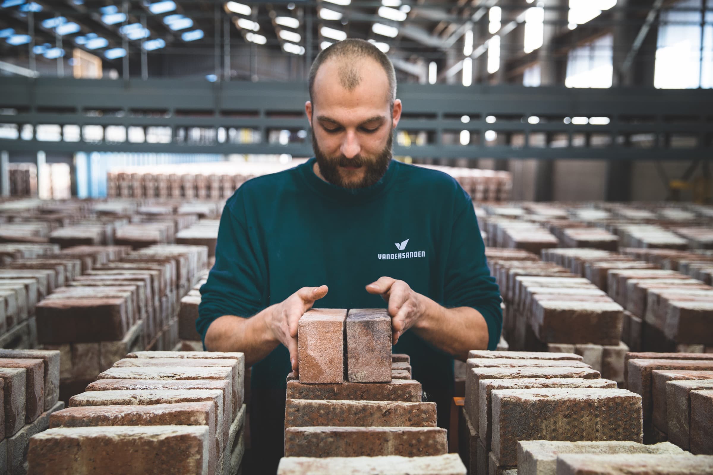 A Vandersanden worker inspecting freshly stacked bricks on the factory floor.